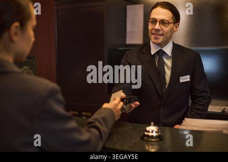 Il giovane receptionist dell'hotel consegna la tessera chiave agli ospiti Foto Stock