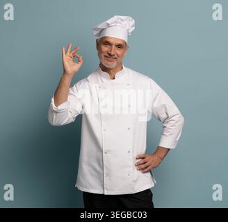 Ritratto di un cuoco sorridente che mostra un segno di ok isolato su sfondo blu Foto Stock