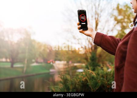 Una donna tiene in mano uno smartphone che mostra una schermata "nessun segnale" in un parco, che illustra una scarsa connessione cellulare, problemi di rete o un'interruzione di Internet mobile Foto Stock