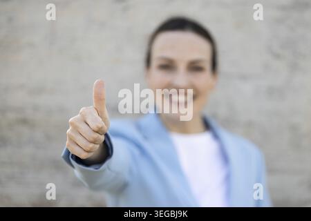 Donna d'affari che mostra il pollice mentre sorride e indossa una giacca blu Foto Stock