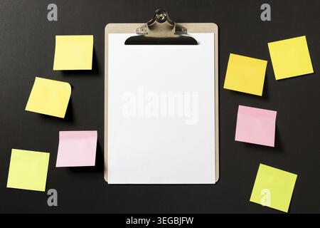 White weisses Papier auf Klemmbrett mit bunten Haftnotizen auf dunklem Hintergrund. Vorlage Mock Up Foto Stock
