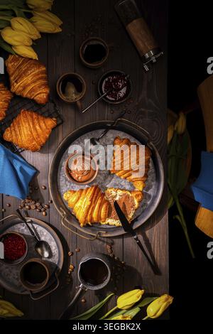 Croissant a colazione con caffè, marmellata e spalmati su un tavolo rustico Foto Stock