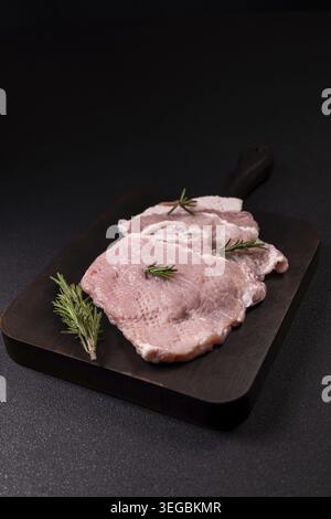 Filetto di maiale crudo con rosmarino fresco su un tagliere di legno scuro, pronto per la cottura, carne rossa cruda preparata per la preparazione dei pasti in stile studio c Foto Stock