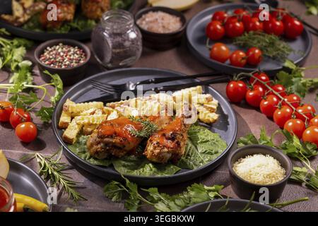 Cosce di pollo arrosto condite con erbe aromatiche e salsa, servite con patatine fritte croccanti su un letto di verdure fresche, accompagnate da ciliegie mature tom Foto Stock