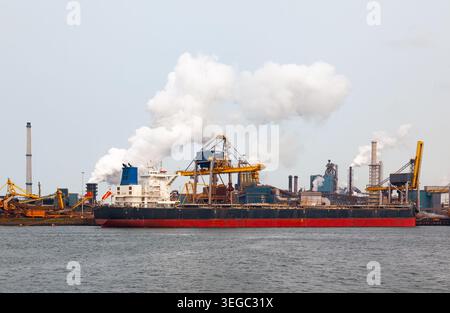 Nave portarinfuse di grandi dimensioni attraccata presso il terminal portuale industriale con camini di fabbrica fumatori e gru cargo a eemshaven nei paesi bassi Foto Stock