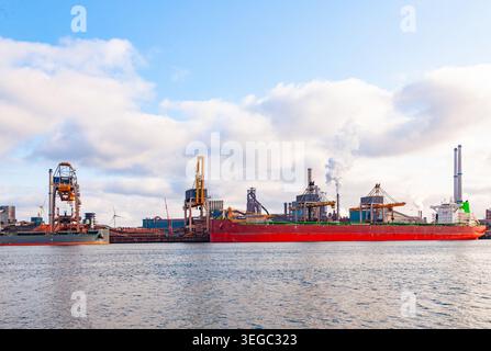Nave portarinfuse di grandi dimensioni attraccata al terminal portuale industriale con gru cargo e camini di fabbrica a eemshaven, nei paesi bassi Foto Stock