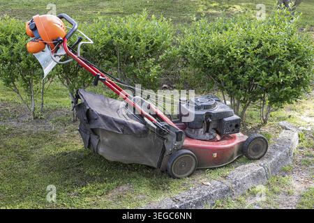 Rasaerba e casco di sicurezza con visiera protettiva e cuffie in giardino Foto Stock