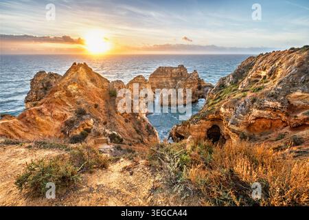 Ponte da Piedade a Lagos, Algarve, Portogallo, all'alba con l'oceano Atlantico, scogliere aspre, faraglioni di mare e luce dorata sulla costa Foto Stock