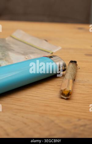 Giunto di marijuana, accendisigari blu e sacchetto di plastica trasparente con cannabis su una superficie di legno Foto Stock