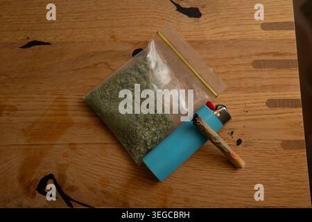 Fiore di cannabis in un sacchetto di plastica con un giunto illuminato e più leggero Foto Stock