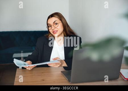 Donna attraente che tiene in mano documenti e lavora con un notebook. Affari. Lavoro d'ufficio. Donna professionista che esamina i documenti. Ritratto di bellezza. Azienda l Foto Stock