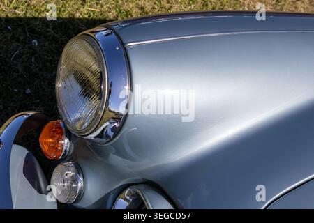 Faro e gruppo indicatori cromati su un'ala blu chiaro di un'auto classica con riflessi alla luce solare intensa Foto Stock