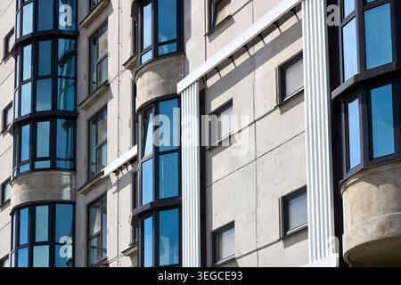 La facciata di un moderno edificio residenziale presenta pareti in cemento grigio con finestre in vetro blu. L'architettura geometrica mostra l'esterno del blocco di appartamenti urbani Foto Stock