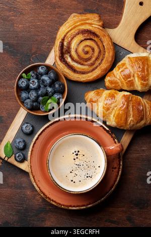 Caffè, cornetti, panini alla cannella e le bacche di prima colazione. Sul tavolo di legno Foto Stock