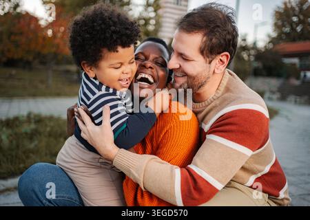 Famiglia multietnica felice con genitori e bambini che si abbracciano all'aperto Foto Stock