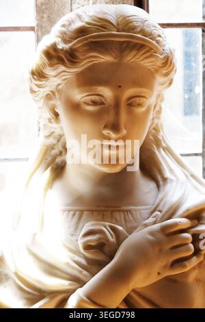 Vista frontale di un classico busto in marmo che raffigura una donna serena con capelli ondulati illuminati da una luminosa finestra da dietro. Foto Stock