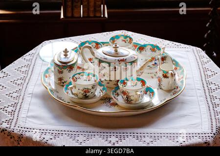 Un dettagliato primo piano di un set da tè in porcellana antico disposto su un vassoio da portata coordinato, il tutto poggiato su una tovaglia bianca in pizzo a crochet. Foto Stock