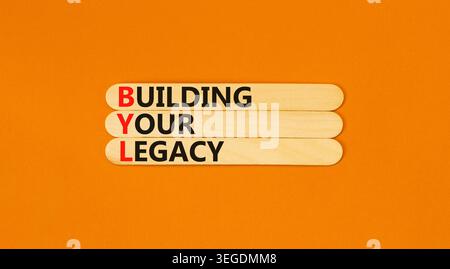 BYL sta costruendo il tuo simbolo legacy. Parole concettuali BYL costruisce la tua eredità su bellissimi bastoncini di legno. Bellissimo sfondo arancione. Business BYL Building Foto Stock