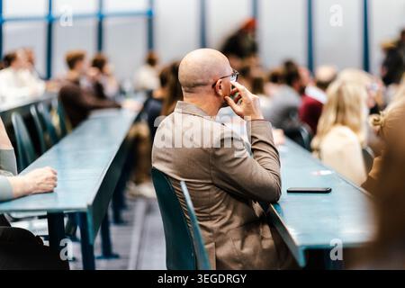 Un grande gruppo di persone diverse che partecipano a una presentazione professionale o a un workshop educativo in una moderna sala conferenze. Concentrati sul pubblico da dietro. Foto Stock