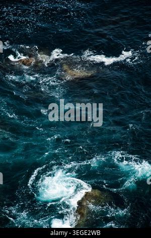 Paesaggio marino naturale con onde oceaniche che si infrangono contro le rocce costiere. L'immagine cattura le consistenze di acqua e pietra, con un'atmosfera intensa. Foto Stock
