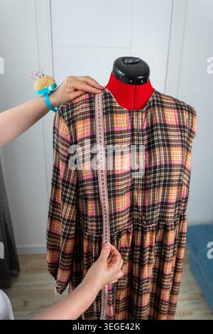 Vista verticale della donna che esegue misurazioni su manichino sartoriale professionale durante il processo di sartoria e cucitura in atelier. Stilista di moda che lavora Foto Stock
