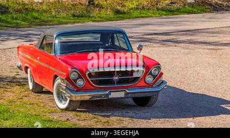 Chrysler 300 cabriolet d'epoca rossa parcheggiata da una strada rurale al sole primaverile, Kinnekulle, Västra Götaland, Svezia. Foto Stock