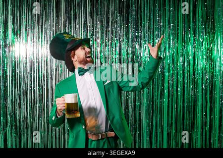 Uomo divertente che si diverte alla festa di San Patrizio con un bicchiere di birra sullo sfondo delle feste Foto Stock