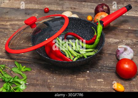 Preparazione di un pasto di famiglia con verdure al vapore in uno Skillet ricoperto di vetro su un tavolo di legno Foto Stock