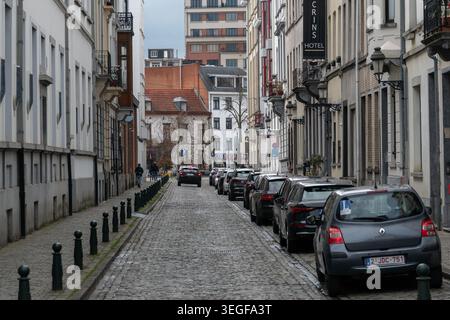 Bruxelles, Belgio - 2 aprile 2026: Le strade acciottolate mostrano auto parcheggiate, dissuasori, insegne dell'hotel e dense facciate storiche in una stretta prospettiva urbana Foto Stock
