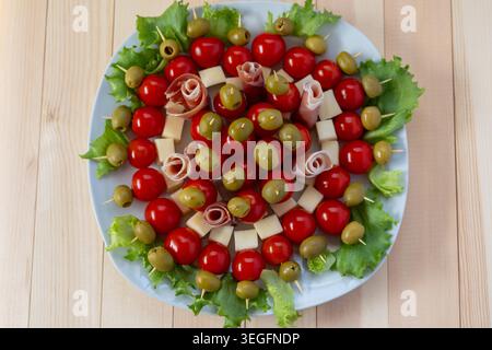 Una fotografia piatta professionale di un piatto bianco rotondo pieno di antipasti festivi. Ogni spiedino include pomodori ciliegini maturi, olive verdi e che Foto Stock