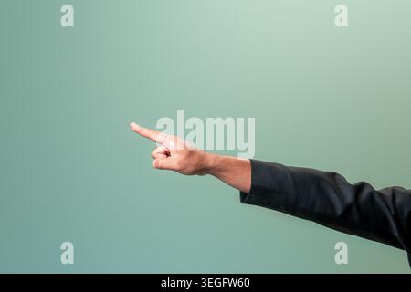 Il braccio di un uomo indonesiano professionista in completo nero che punta l'indice verso sinistra su uno sfondo verde pulito. Foto Stock