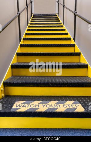 Scala industriale gialla e nera con gradini in metallo antiscivolo e corrimano protettivi per un accesso sicuro all'interno del luogo di lavoro o del magazzino Foto Stock