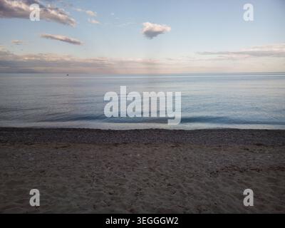 Un tranquillo e sereno paesaggio marino al tramonto caratterizzato da morbide increspature che si gettano su una spiaggia sabbiosa e ciottolosa sotto un calmo cielo serale. Foto Stock