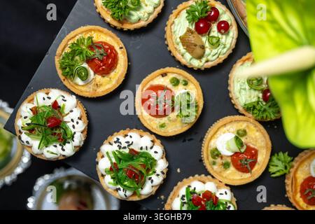 Un piatto con vista dall'alto offre vari antipasti gourmet, crostate e mini quiche servite su un piatto nero. Foto Stock