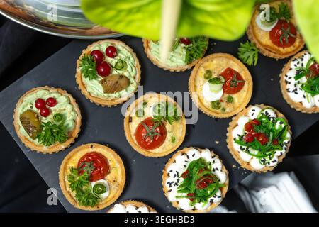 Un piatto con vista dall'alto offre vari antipasti gourmet, crostate e mini quiche servite su un piatto nero. Foto Stock