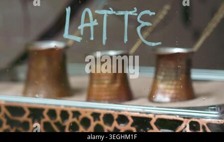 Tre pentole di rame per preparare caffè turco dietro una finestra con il segno del latte Foto Stock