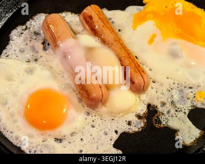 Primo piano di uova fritte e salsicce cucinate in padella. Preparazione della colazione fatta in casa con cibi proteici per un pasto veloce. Foto Stock