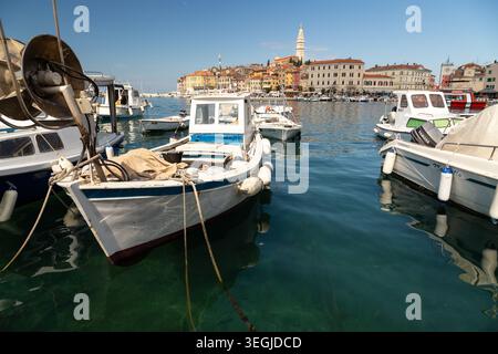 Piccole barche da pesca ancorate nel porto di Rovigno con edifici storici e una torre di chiesa sullo sfondo. Foto Stock