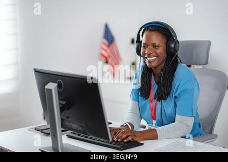 Donna nera sorridente che indossa la cuffia che usa il computer per la telemedicina Foto Stock