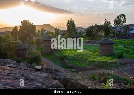 Vista panoramica di Lalibela con caratteristiche case in pietra a due piani e tetti in paglia. La calda luce del tramonto illumina l'erba verde e gli alberi, con l'ingegno Foto Stock