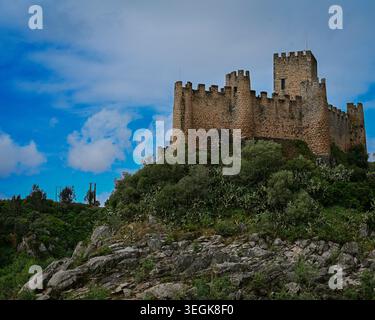 Un suggestivo castello medievale in pietra arroccato in cima a un'aspra collina sotto i suggestivi cieli blu e le torreggianti nuvole. Foto Stock