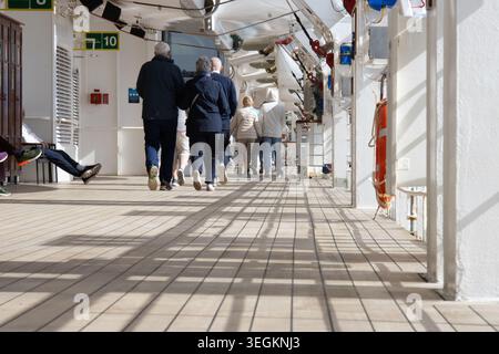 I passeggeri senior camminano lungo il ponte esterno della passeggiata di una nave da crociera in mare. Foto Stock