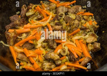 Carne di agnello, cipolle e carote fritte nel tradizionale kazan per la preparazione del plov uzbeko, autentica ricetta della cucina asiatica fatta in casa. Foto Stock
