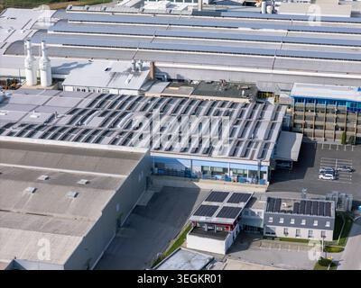 Vista aerea di un grande complesso industriale con pannelli solari sui tetti e area parcheggio visibile nelle vicinanze durante le ore diurne. Foto Stock