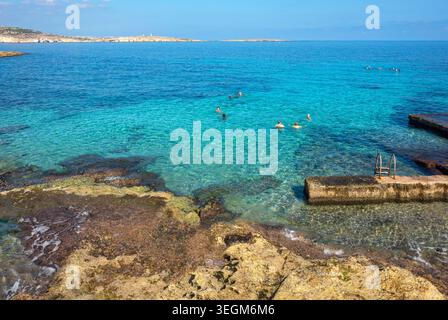 Le persone che si bagnano godendosi l'acqua di mare turchese presso la spiaggia rocciosa naturale sul mare della baia di San Giuliano. Malta Foto Stock
