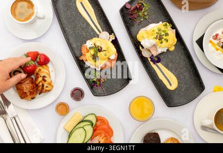 Deliziosa colazione a buffet con uova Benedict e frutta fresca in un accogliente ambiente da caffetteria Foto Stock