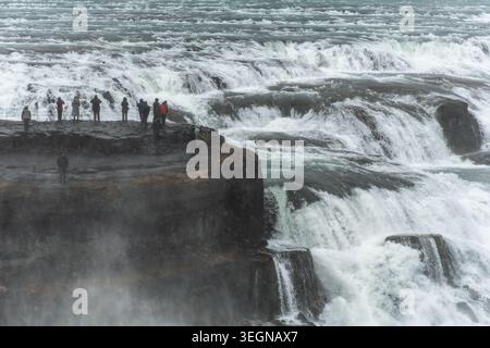 I turisti che osservano le potenti cascate di Gullfoss da una sporgenza rocciosa di osservazione, l'Islanda, l'Europa Foto Stock