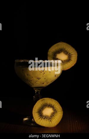 Cocktail di frutta Kiwi servito in un bicchiere con bordo dorato di zucchero e guarnito con fette di kiwi fresche, creando una bevanda rinfrescante su uno sfondo scuro Foto Stock