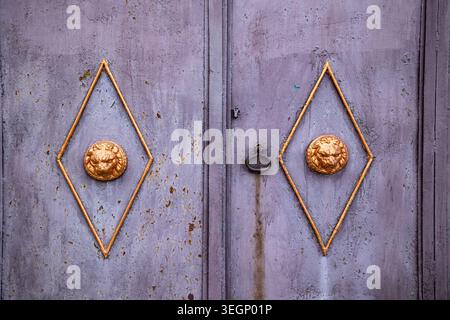Primo piano di una porta in metallo viola intemprato con vernice sfalsata e ruggine, contenente due forme di diamante dorato che racchiudono teste di leone scolpite lungo una Foto Stock