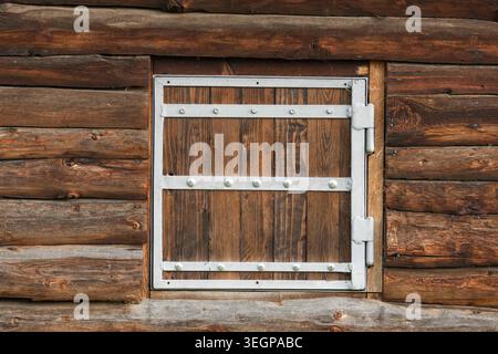 Pareti rustiche in legno della cabina con tradizionale finestra con persiane, dettagli architettonici ravvicinati della facciata in legno intempestivo Foto Stock